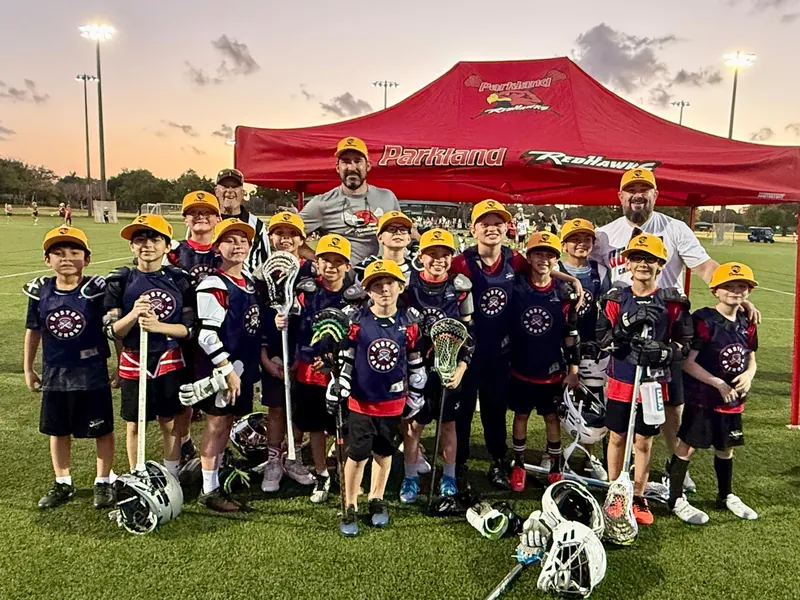 A Redhawks boys team and coaches pose with their sticks under the red Redhawks tent at sunset