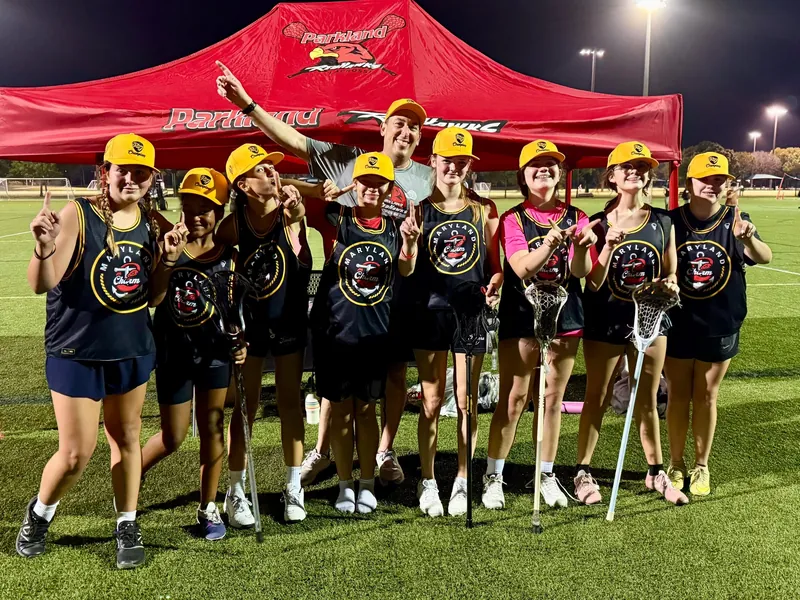 A Redhawks girls team in yellow caps smiles under the red Redhawks tent at night