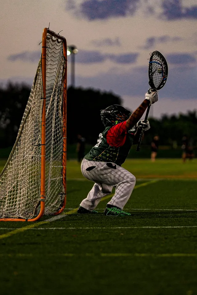 A Redhawks goalie in a helmet makes a save at the net at dusk